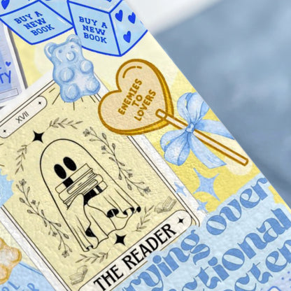 Tarot card with ghost reading books, gummy bear, and "Enemies to Lovers" heart.