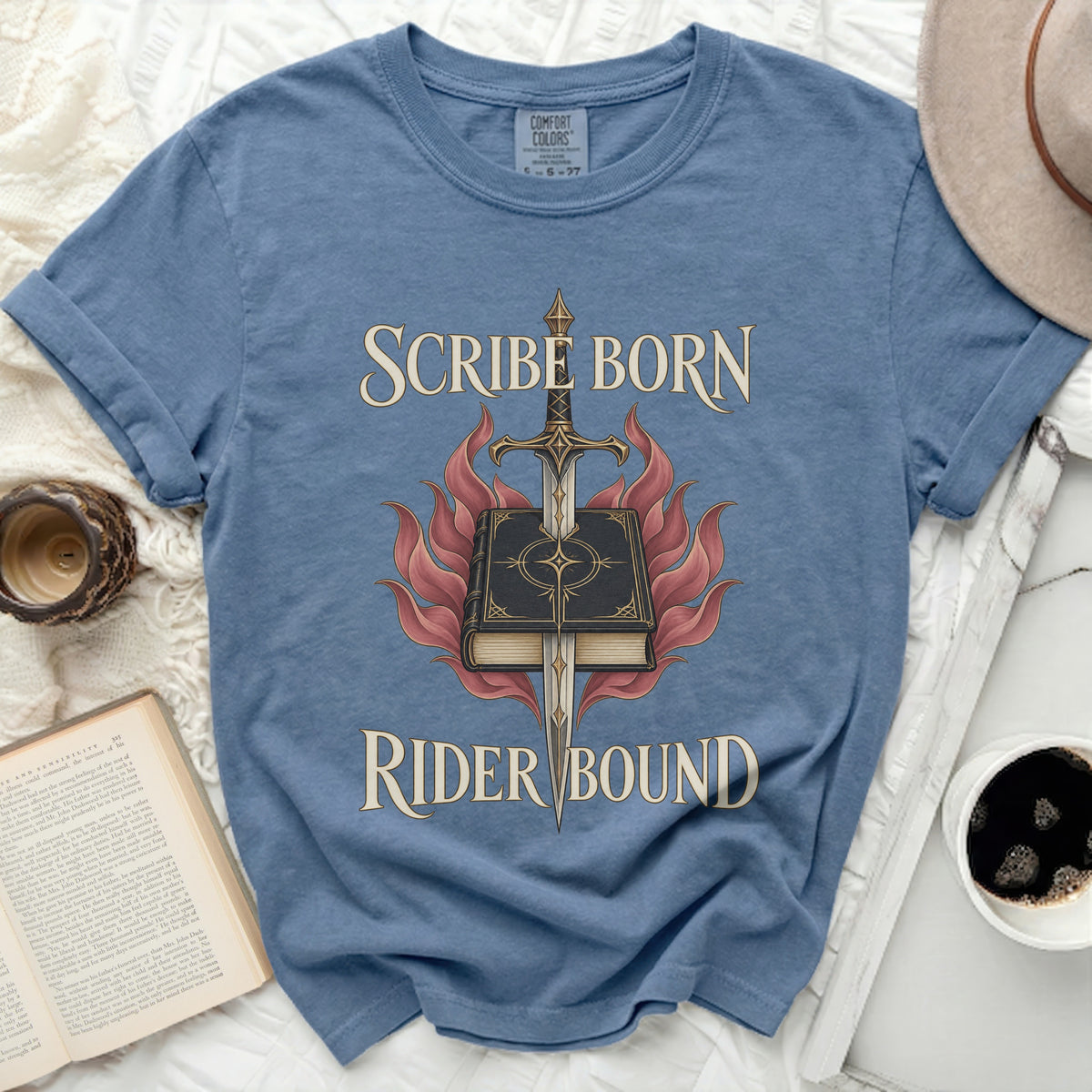 Blue crewneck t-shirt featuring the text Scribe Born Rider Bound surrounding an illustration of a sword piercing a book amidst flames.