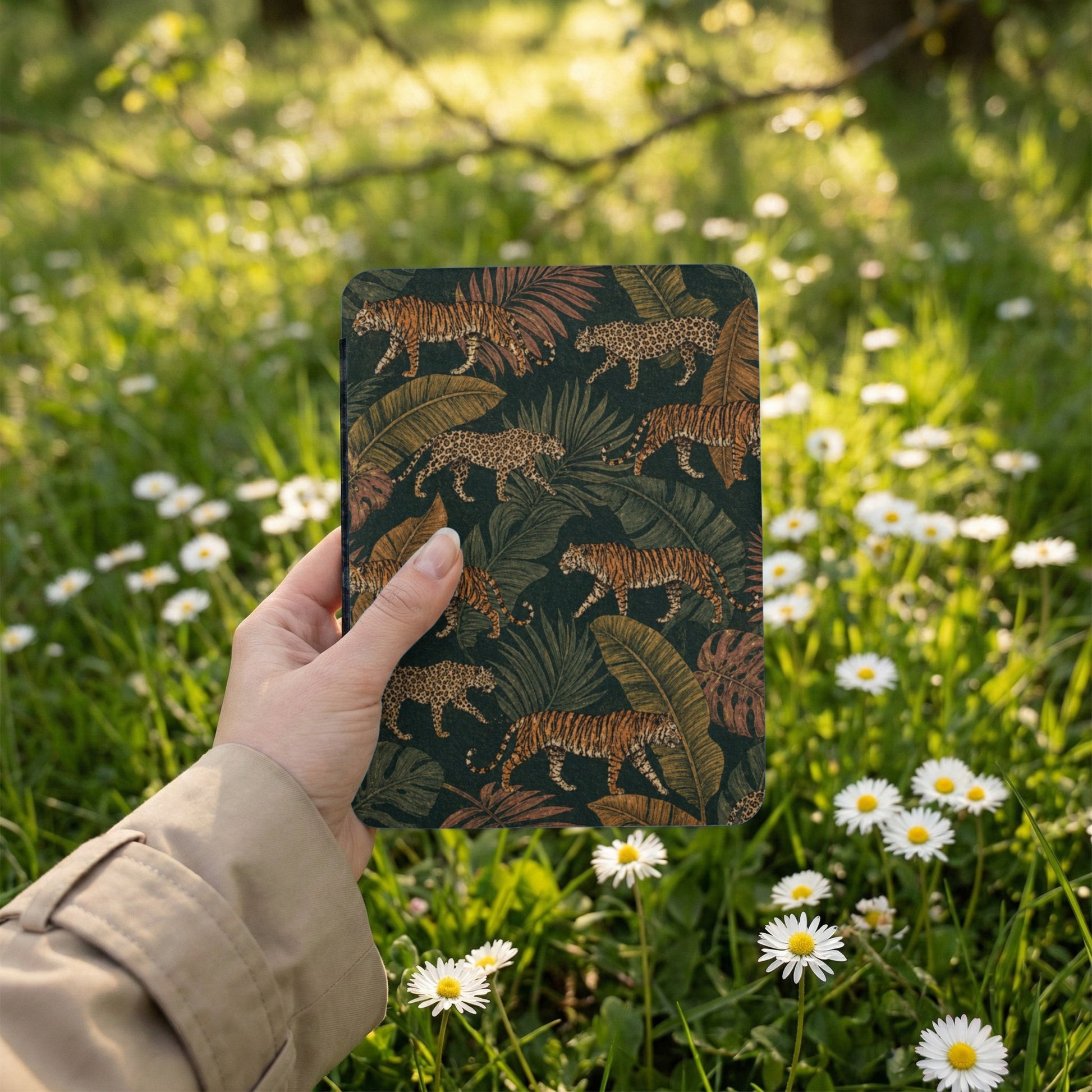 Hand holding a case with a tiger and leopard jungle pattern on dark background.