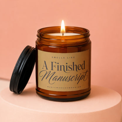 Amber jar candle with lit wick, "Smells Like A Finished Manuscript" text.