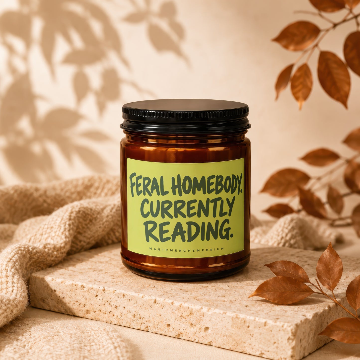 Amber jar candle with green label reading "FERAL HOMEBODY. CURRENTLY READING."
