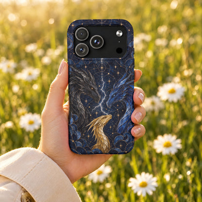 Hand holding a dark blue smartphone case featuring celestial dragons and lightning against a daisy-filled meadow.
