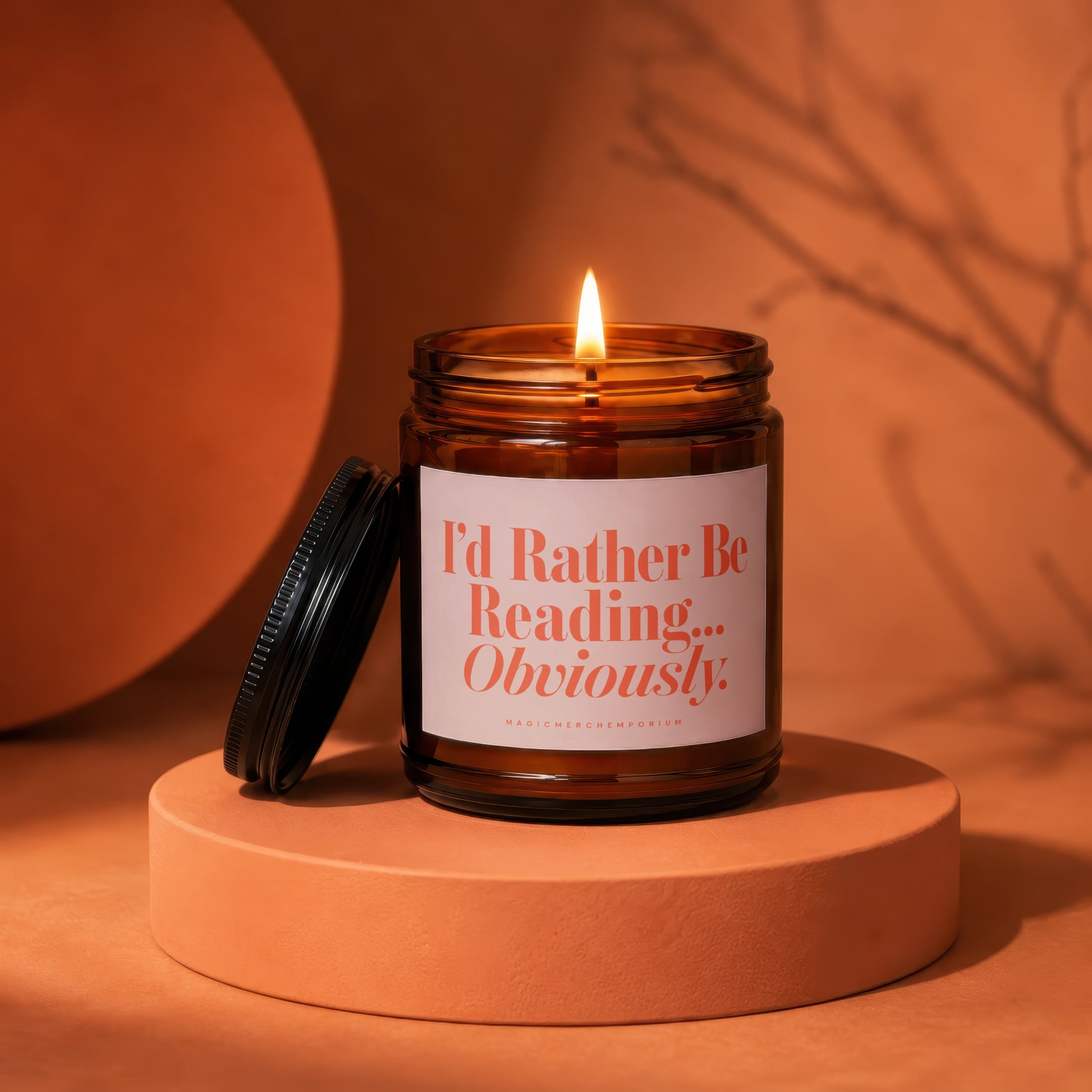 Amber jar candle with lit wick and label reading "I'd Rather Be Reading... Obviously."