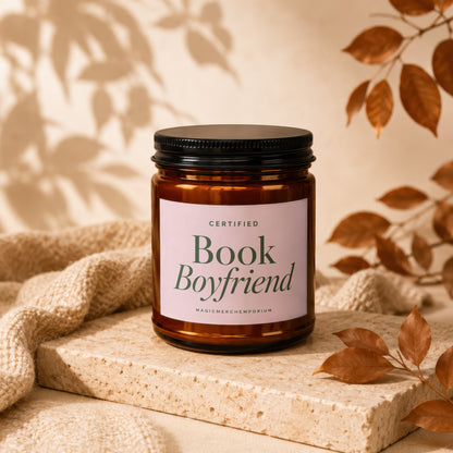 Amber glass candle with black lid, "Certified Book Boyfriend" label, on stone.