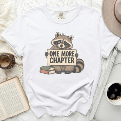 White t-shirt with a raccoon holding a sign that says "ONE MORE CHAPTER".