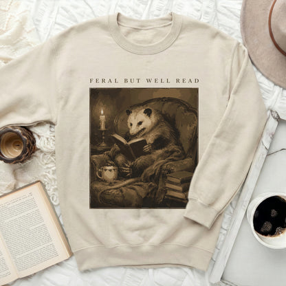 Sweatshirt with a graphic of an opossum reading a book with text "FERAL BUT WELL READ".