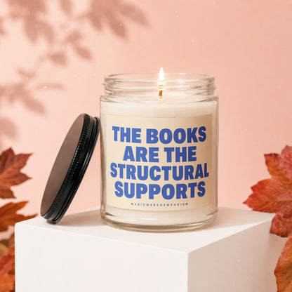 Lit candle in glass jar with lid off reading "THE BOOKS ARE THE STRUCTURAL SUPPORTS"