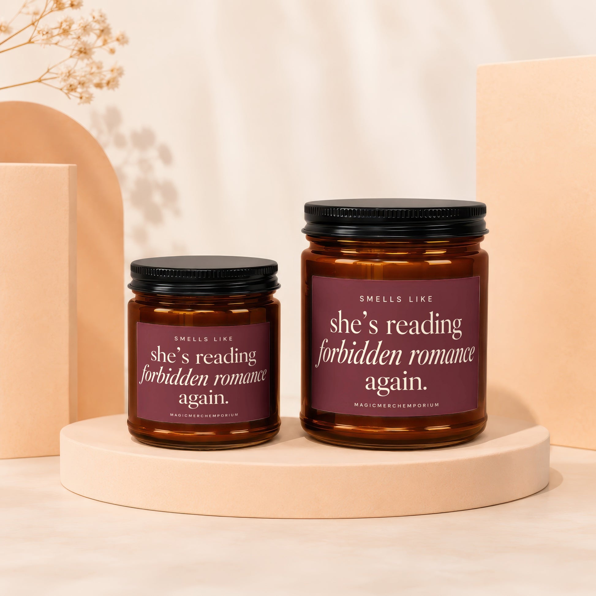 Two amber glass candles with maroon labels reading "she's reading forbidden romance again."