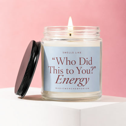 Jar candle with lit wick, black lid, and label saying "Smells Like 'Who Did This to You?' Energy MAGICMERCH)EMPORIUM".