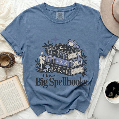 Blue t-shirt with a graphic of spellbooks, a frog, candle, mushrooms, and text "i love Big Spellbooks".