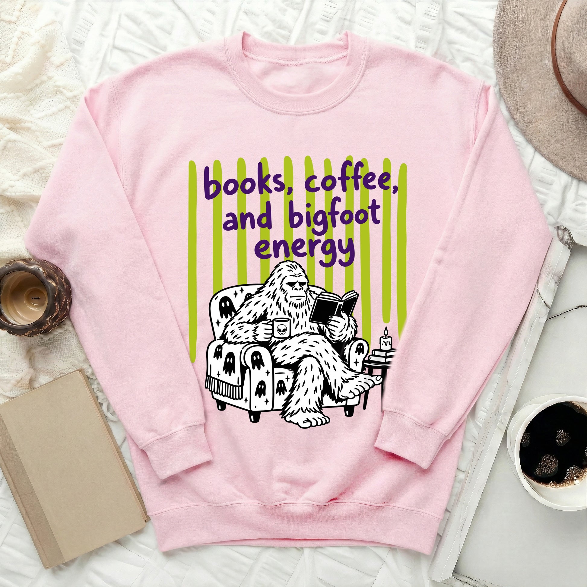 Pink sweatshirt with Bigfoot reading and drinking coffee, saying "books, coffee, and bigfoot energy."