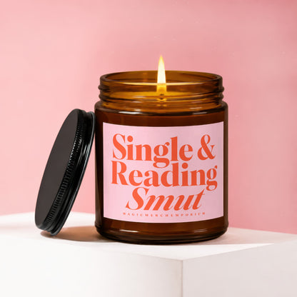 Brown glass candle with lit wick and pink label reading "Single & Reading Smut."