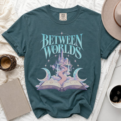 Teal t-shirt with "BETWEEN WORLDS" text over fantasy castle, moons, and open book.