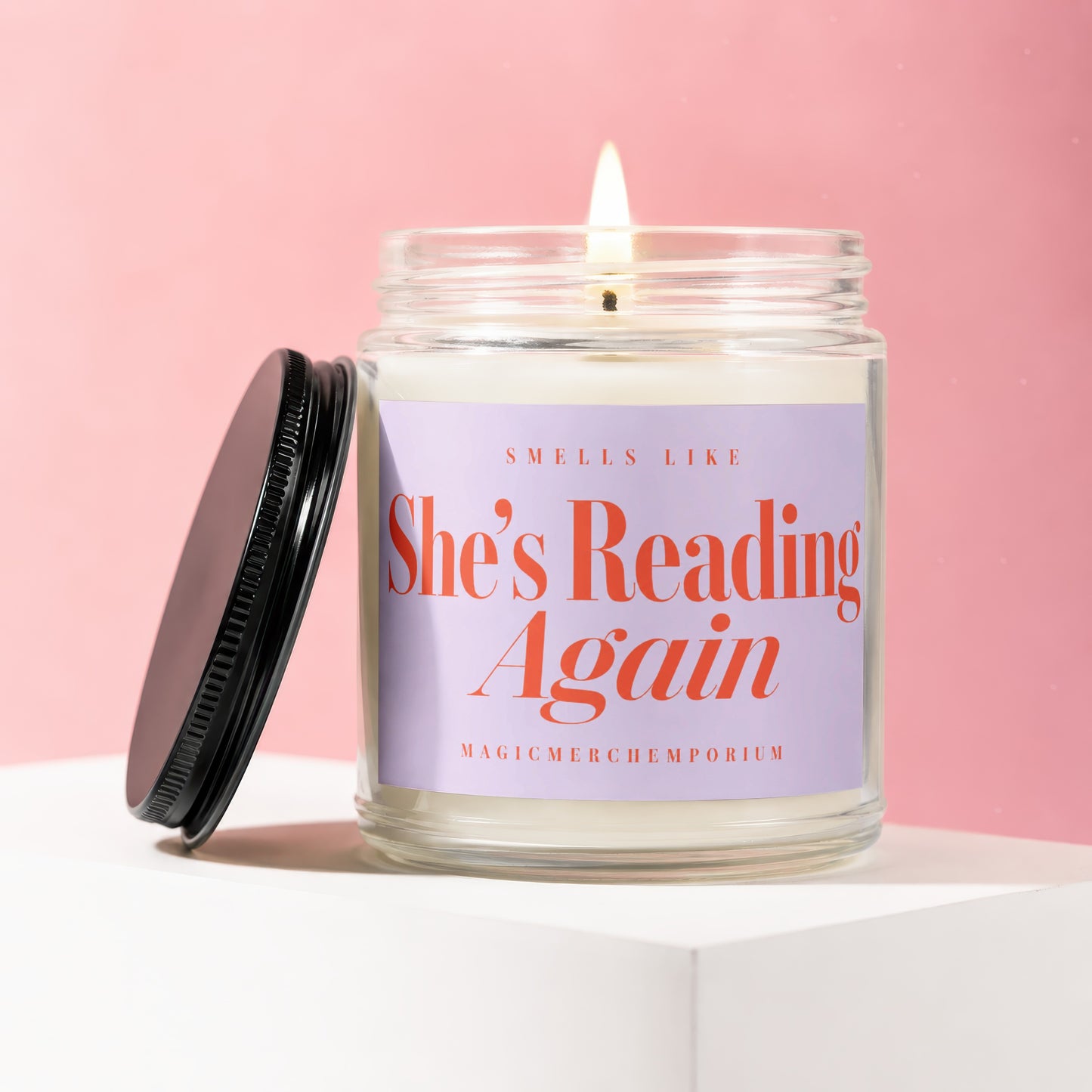 Candle with lit wick, reading "Smells Like She's Reading Again".