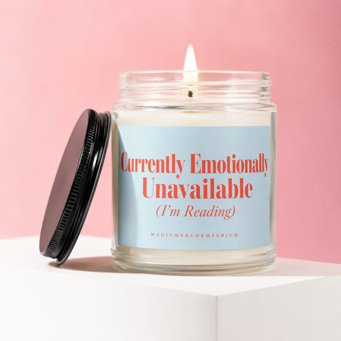 Glass candle with burning wick, light blue label reading "Currently Emotionally Unavailable (I'm Reading)".