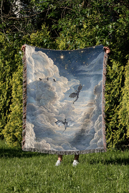 A person is holding up a large, colorful blanket with a dragon and clouds design, standing in a grassy area surrounded by trees.