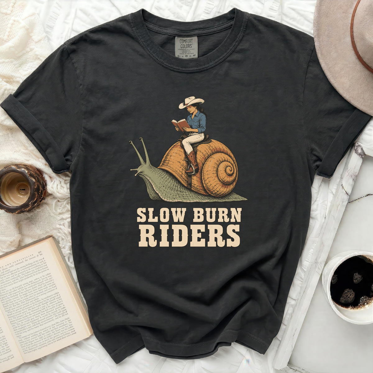 Woman in cowboy hat riding a snail, "Slow Burn Riders" text.