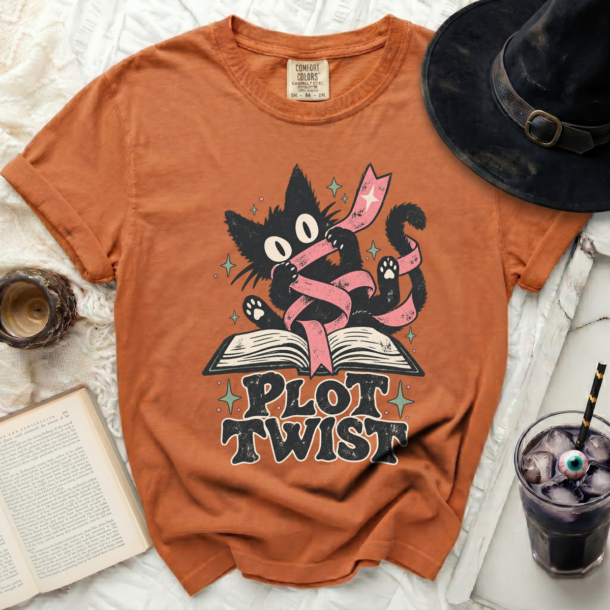 Orange t-shirt with black cat and ribbon graphic on an open book with text "PLOT TWIST".