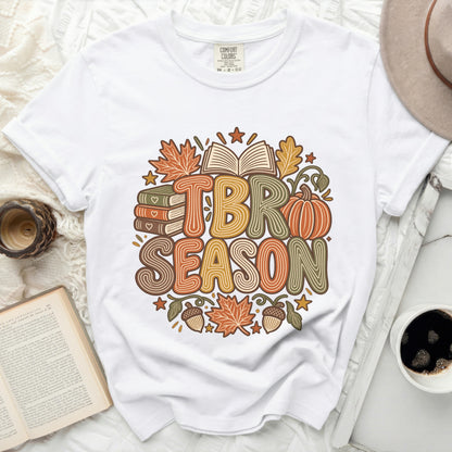 White t-shirt with "TBR SEASON" text surrounded by autumn leaves, books, and a pumpkin.