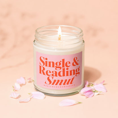 Candle with lit wick and pink label saying "Single & Reading Smut"