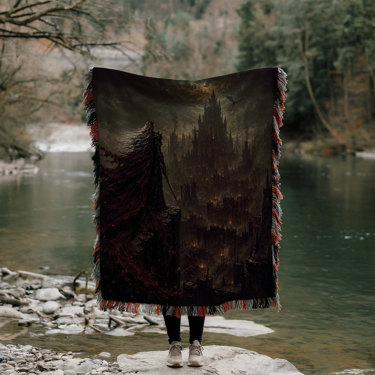 A person stands on a rock, holding a large, dark-colored blanket that features a castle-like structure on it. The person is positioned in front of a body of water, with trees and foliage visible in the background.