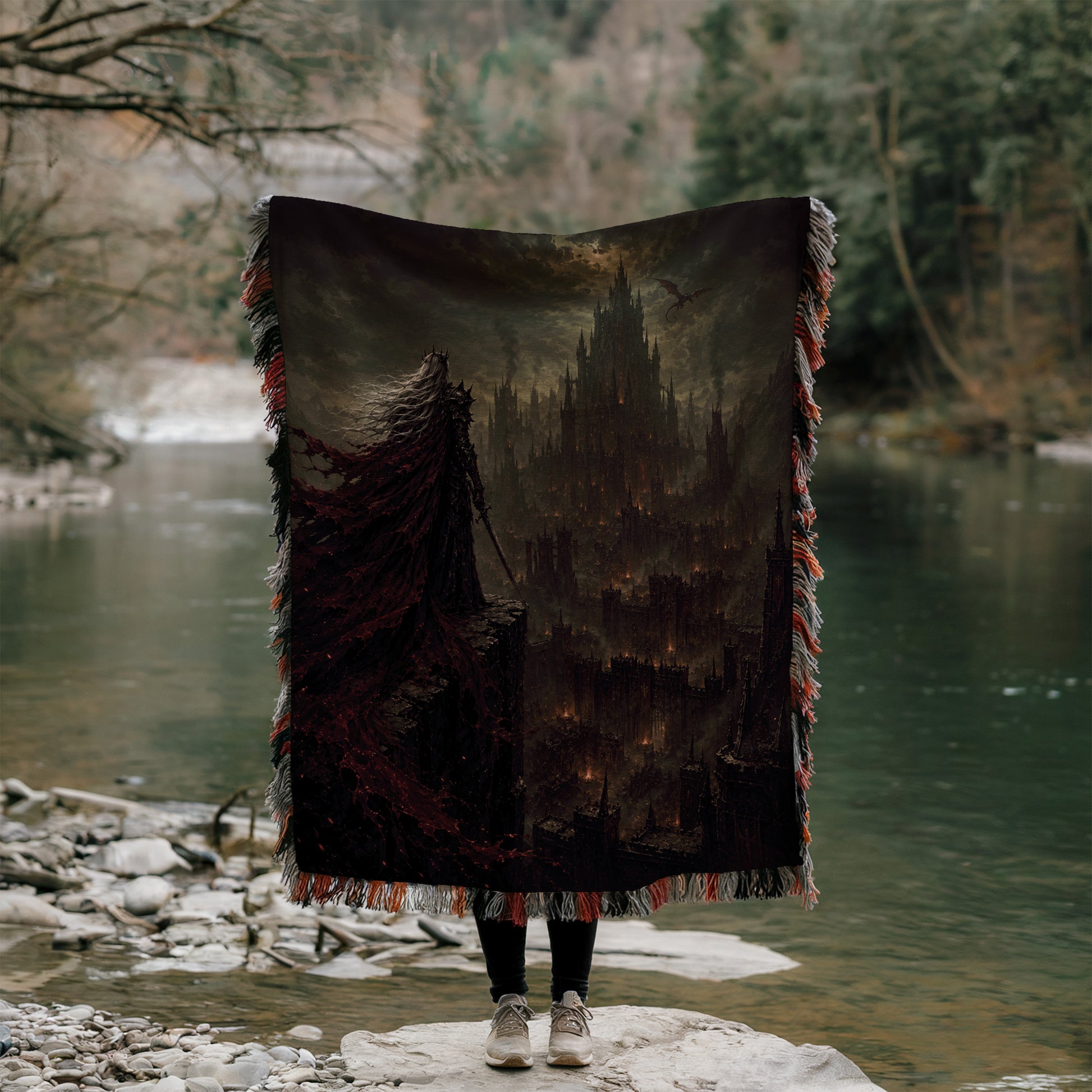 A person stands on a rock, holding a large, dark-colored blanket that features a castle-like structure on it. The person is positioned in front of a body of water, with trees and foliage visible in the background.