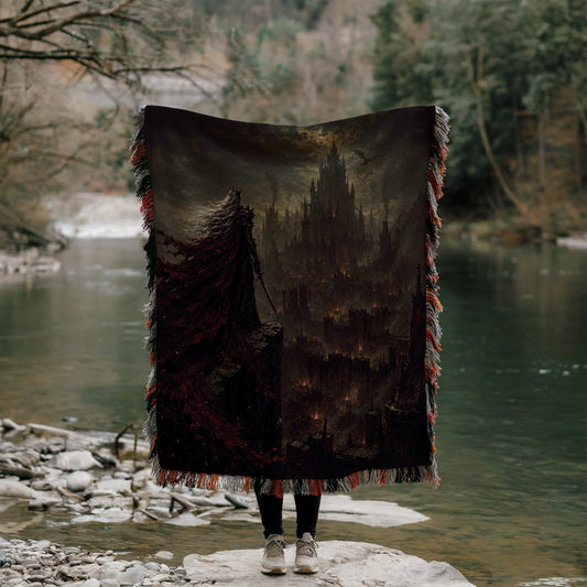 A person stands on a rock, holding a large, dark-colored blanket that features a castle-like structure on it. The person is positioned in front of a body of water, with trees and foliage visible in the background.