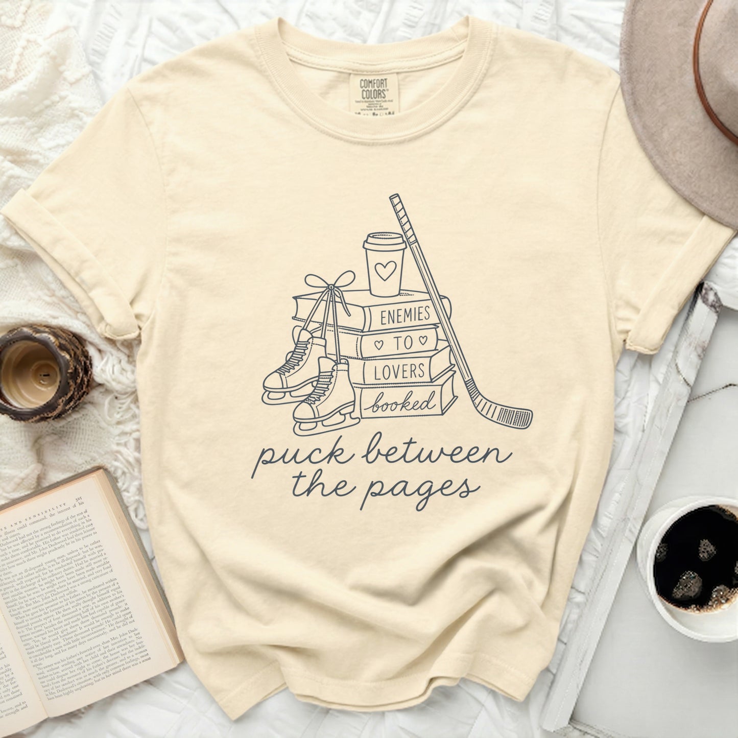 T-shirt with books, skates, and hockey stick, reading "enemies to lovers puck between the pages".