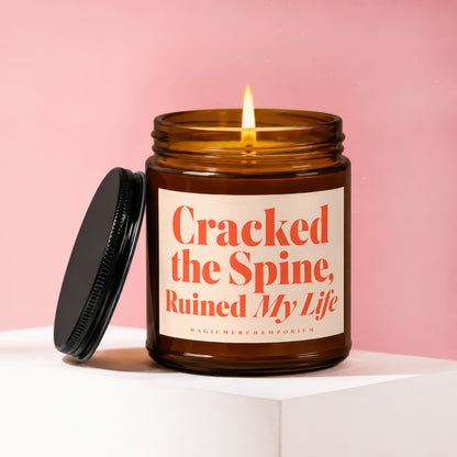 Brown glass candle with lit flame and black lid, labeled "Cracked the Spine, Ruined My Life."