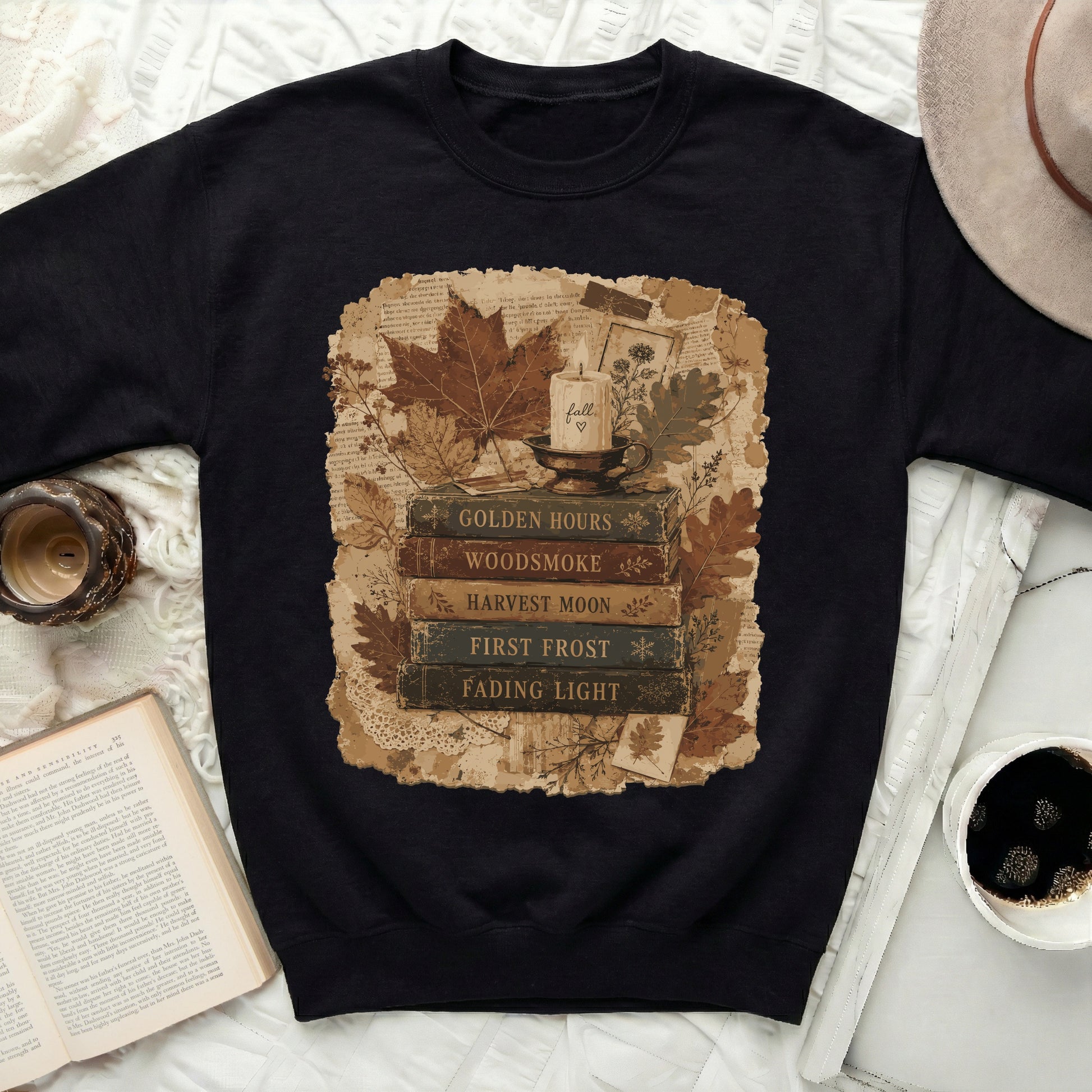 Black sweatshirt with fall-themed graphic featuring stacked books, a candle, and autumn leaves.