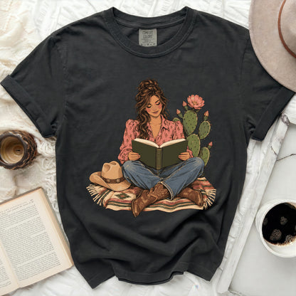 Comfort Colors graphic t-shirt featuring a woman reading by a cactus and cowboy hat.