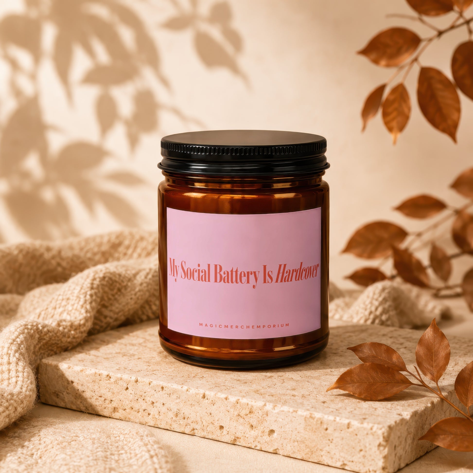 Amber candle in a jar with pink label reading "My Social Battery Is Hardcover".