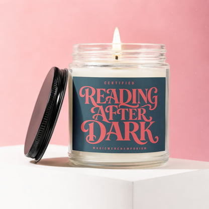 Jar candle lit, with black lid resting nearby, on a white block and pink background.