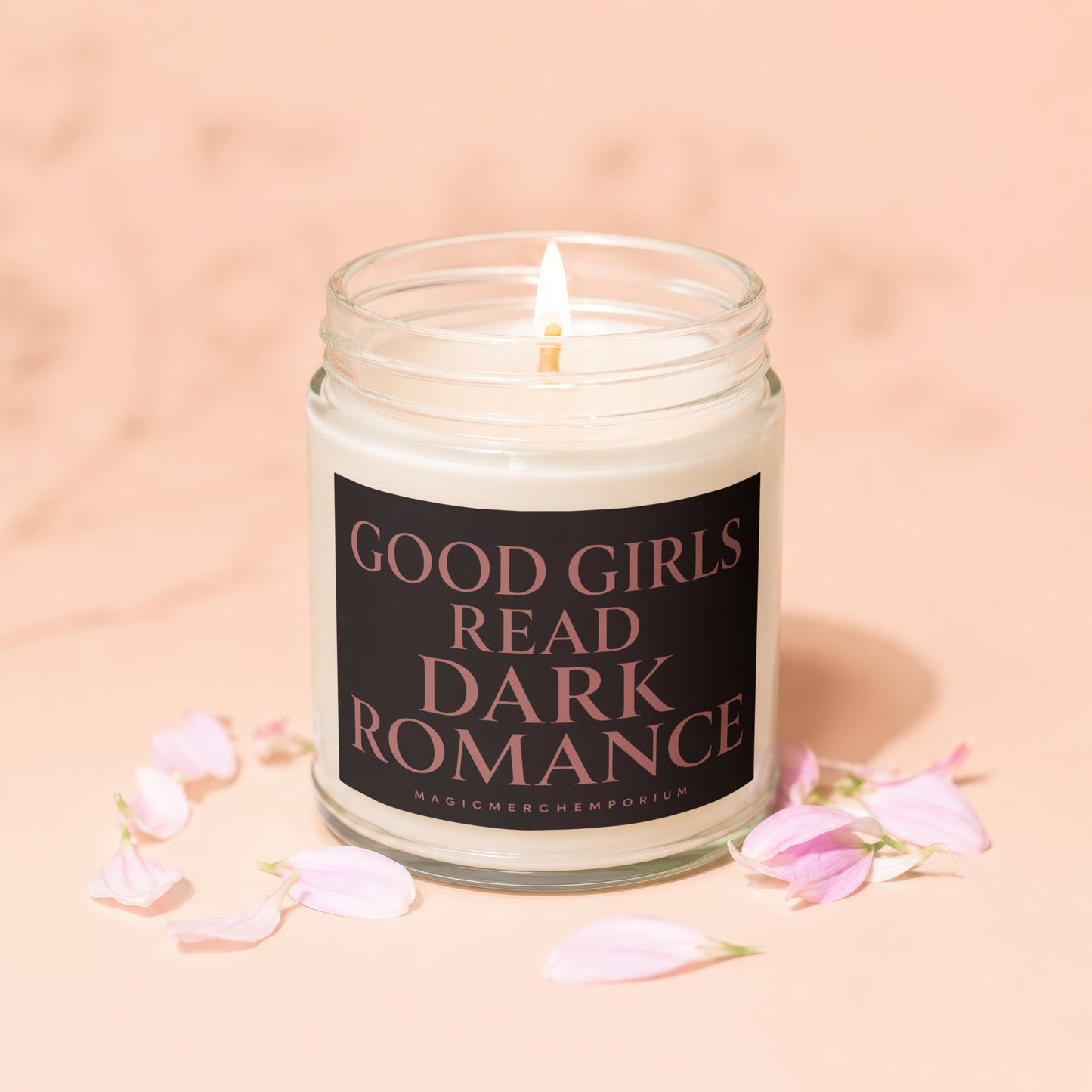 Glass candle with lit wick, featuring a black label with pink text reading "GOOD GIRLS READ DARK ROMANCE".