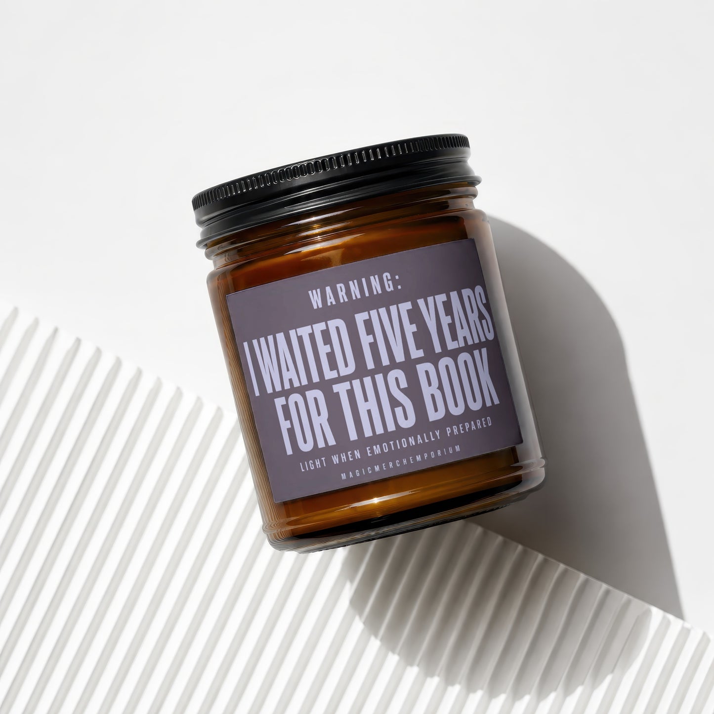 An amber glass candle jar with a black lid and label reading "I waited five years for this book."