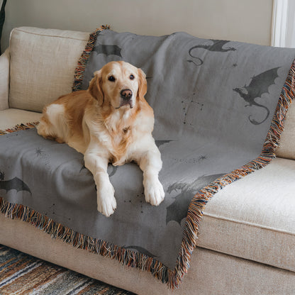 A golden retriever dog is lying on a gray blanket with dragon designs, resting on a beige couch.
