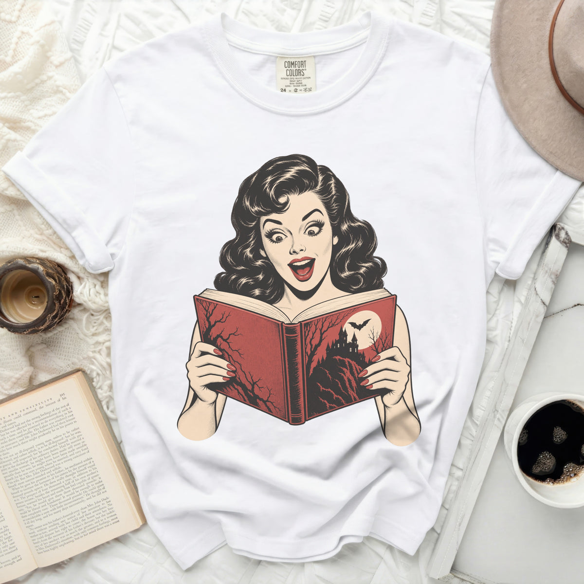 White t-shirt with a vintage comic graphic of a surprised woman reading a spooky book.
