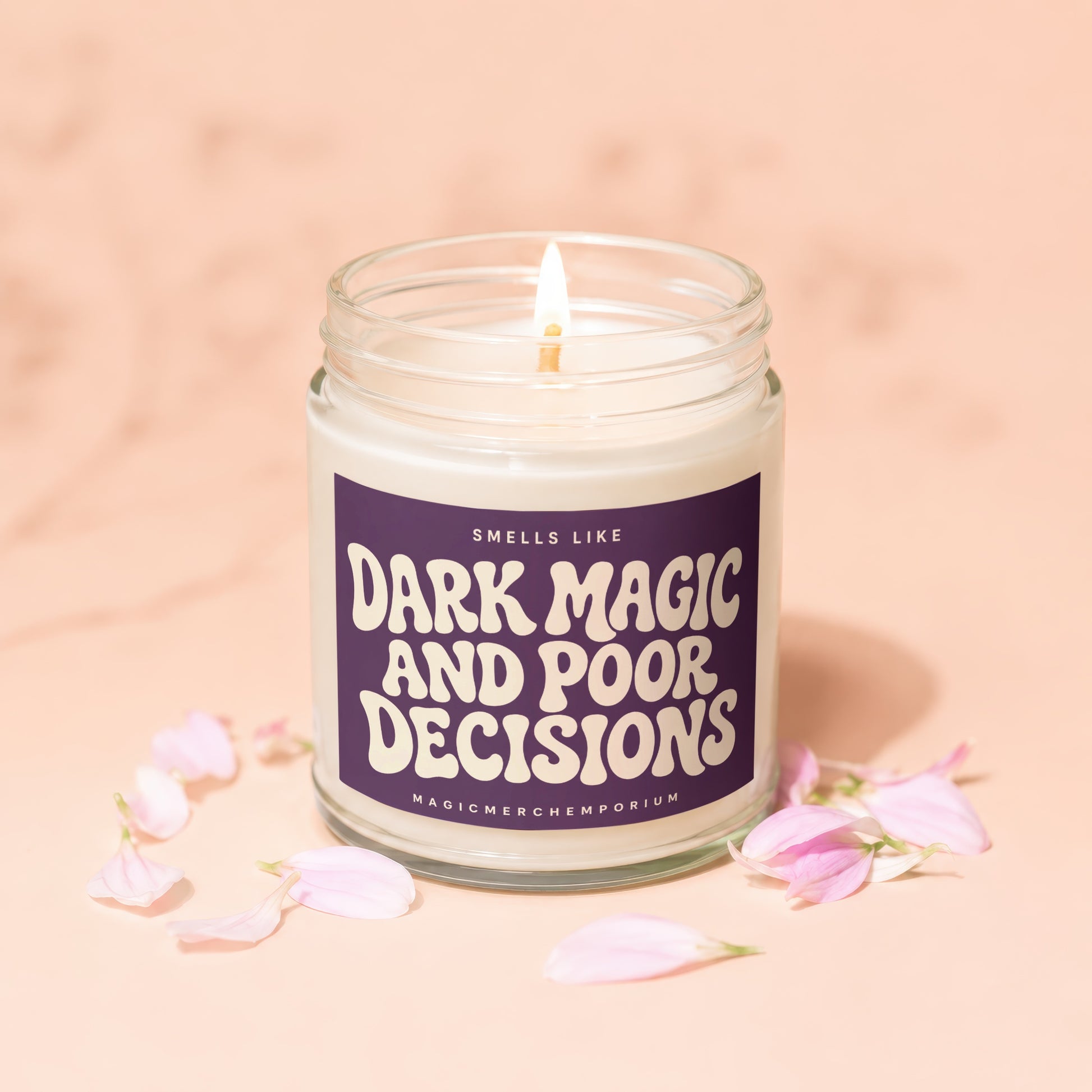 Candle with "Smells Like Dark Magic And Poor Decisions" label and pink petals.