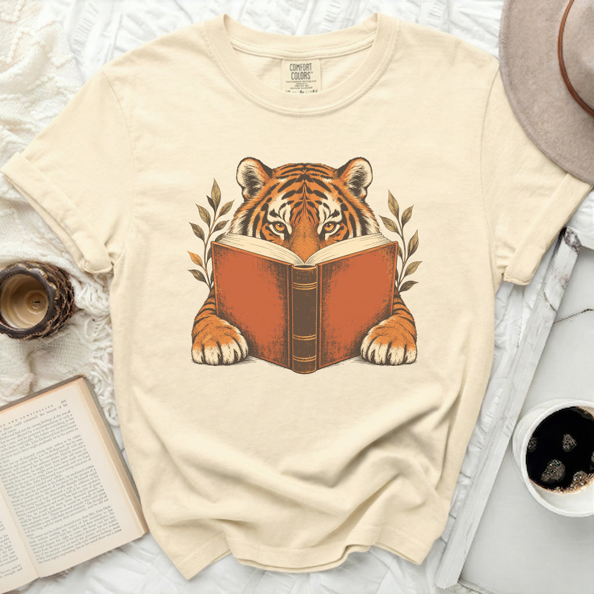 Tiger reading an open book with leaves, printed on a tan t-shirt.