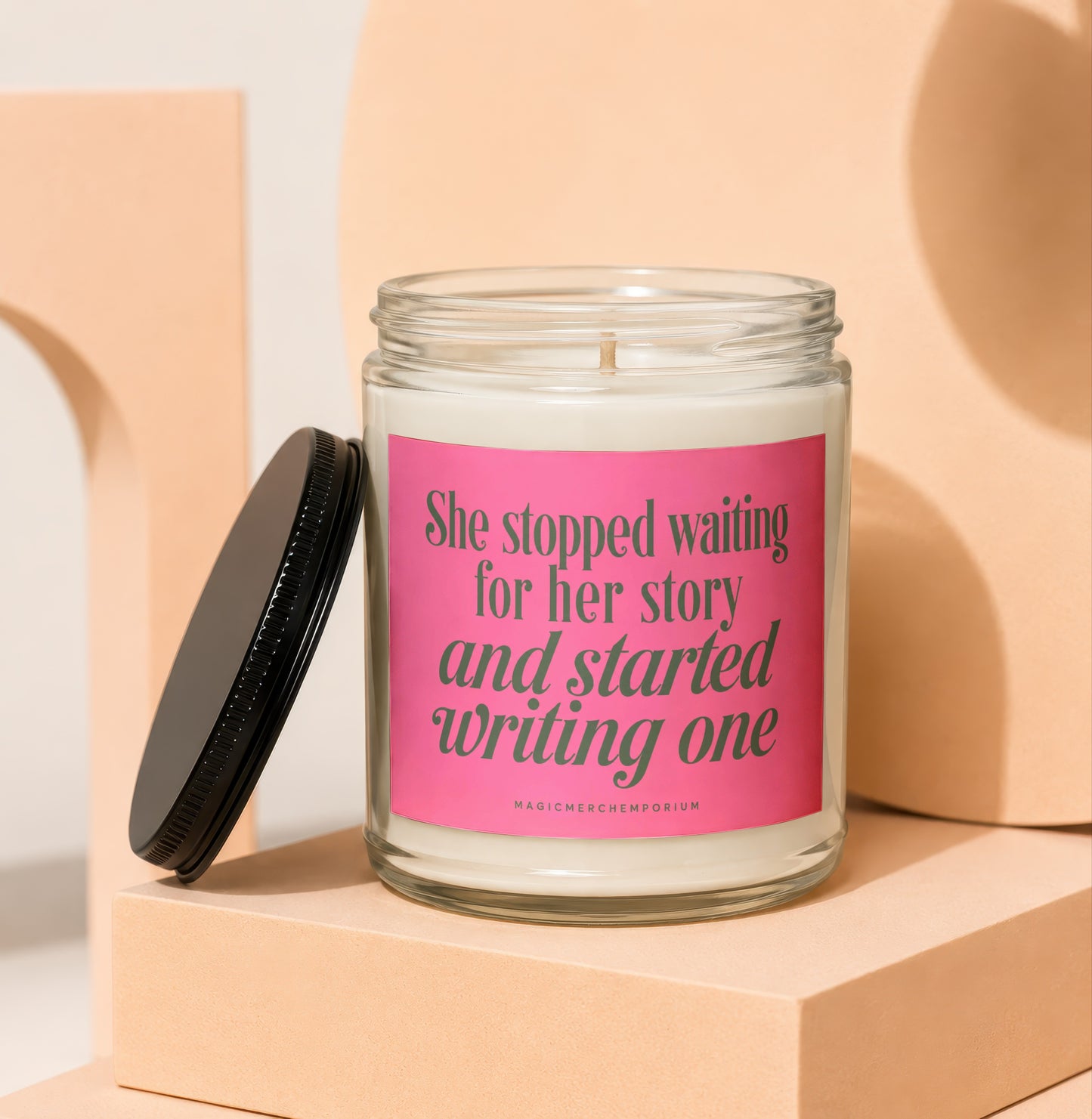 Glass candle with pink label reading "She stopped waiting for her story and started writing one."
