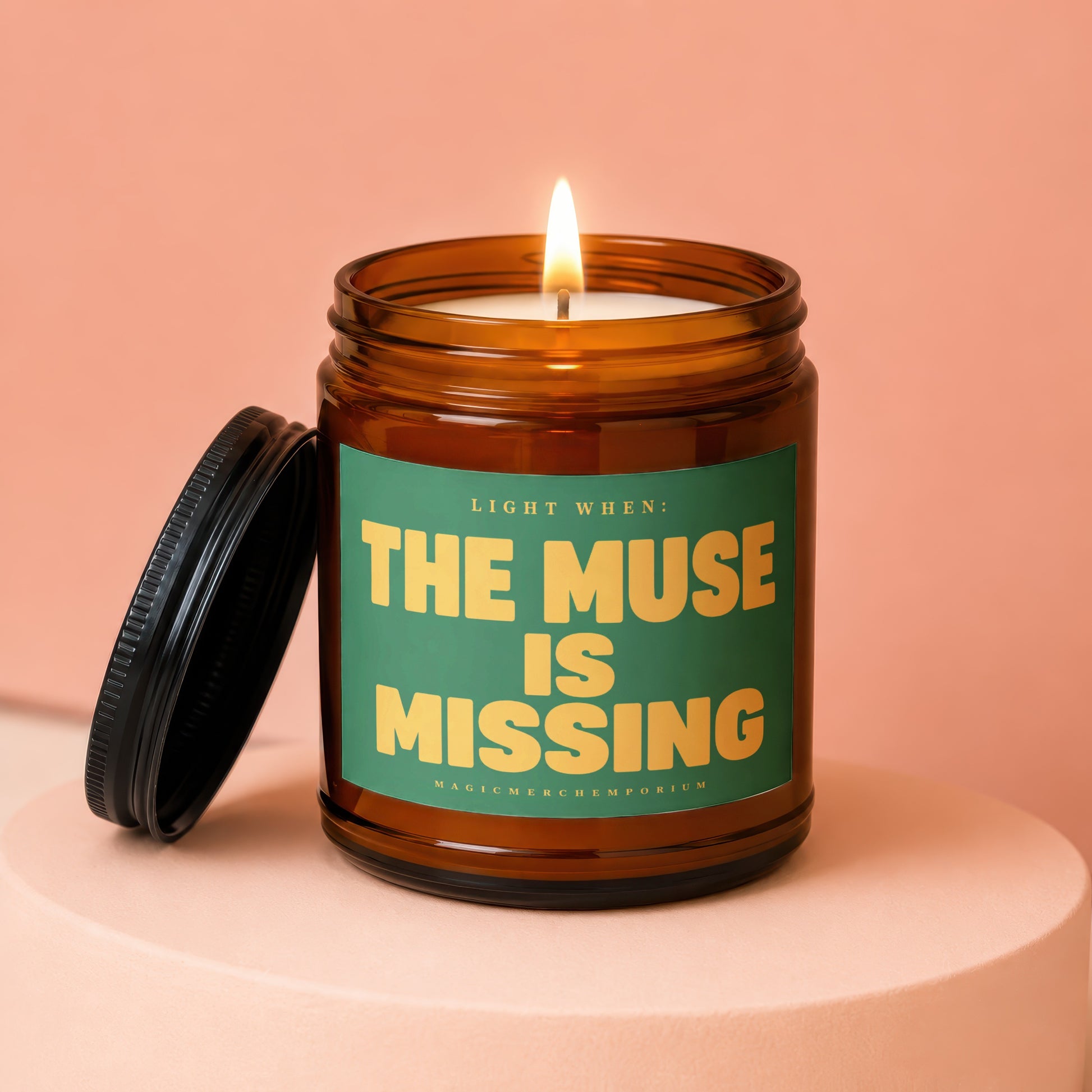 Lit amber jar candle with green label reading "THE MUSE IS MISSING".