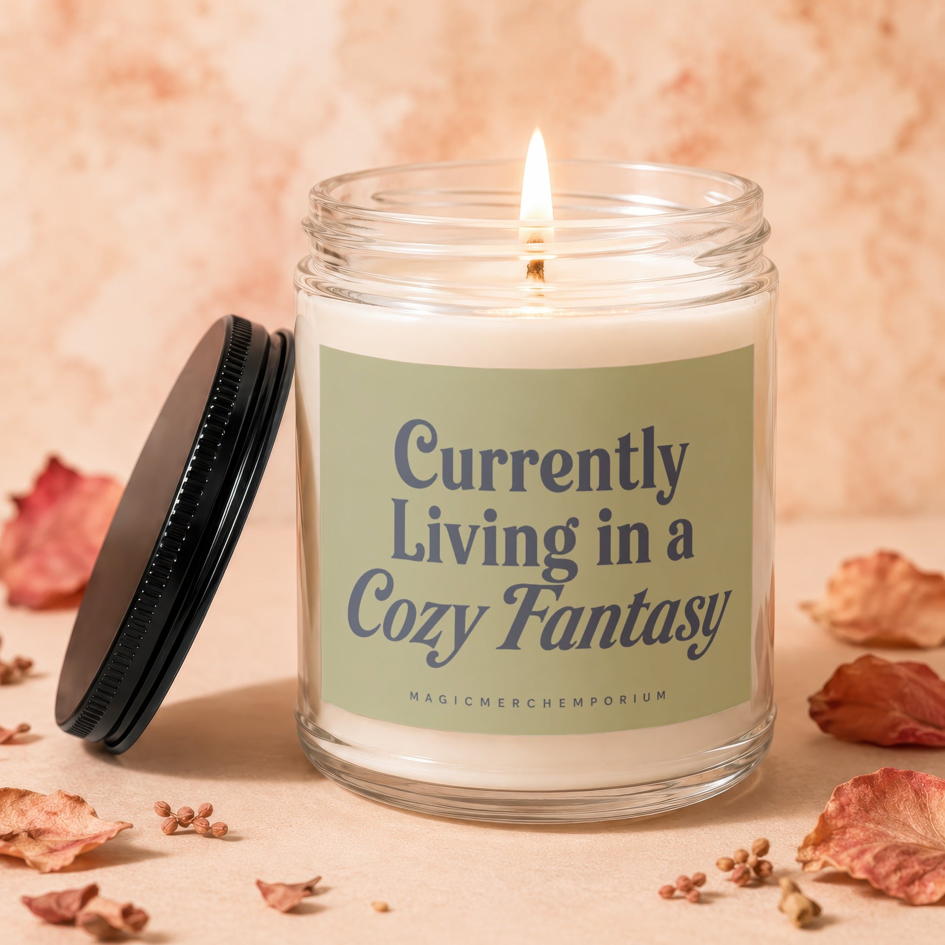 Glass jar candle with lit wick, black lid, and text "Currently Living in a Cozy Fantasy".