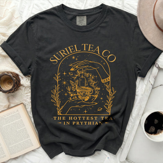 Black t-shirt with yellow graphic of hands holding a teacup and text "SURIEL TEA CO THE HOTTEST TEA - IN PRYTHIAN".