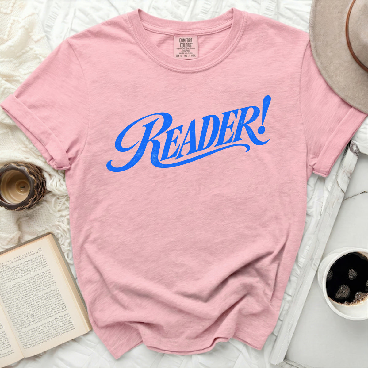 Pink Comfort Colors t-shirt with blue "READER!" graphic on front.