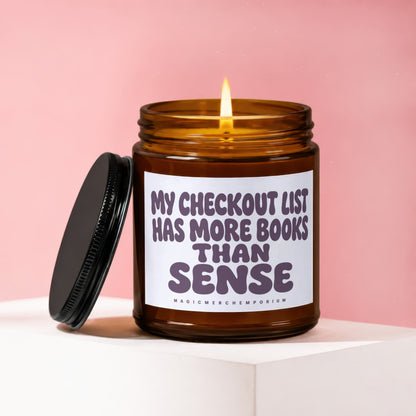 Amber glass candle with lid off, displaying text "MY CHECKOUT LIST HAS MORE BOOKS THAN SENSE".