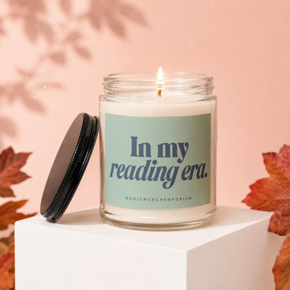 Glass candle with burning wick, lid off, on white cube, text "In my reading era."