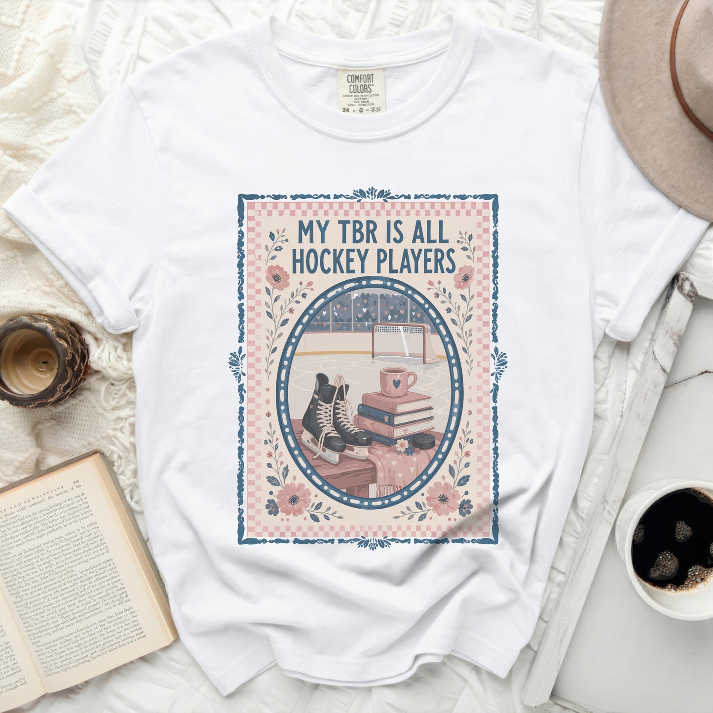 White t-shirt with a graphic of hockey rink, skates, books, and flowers.