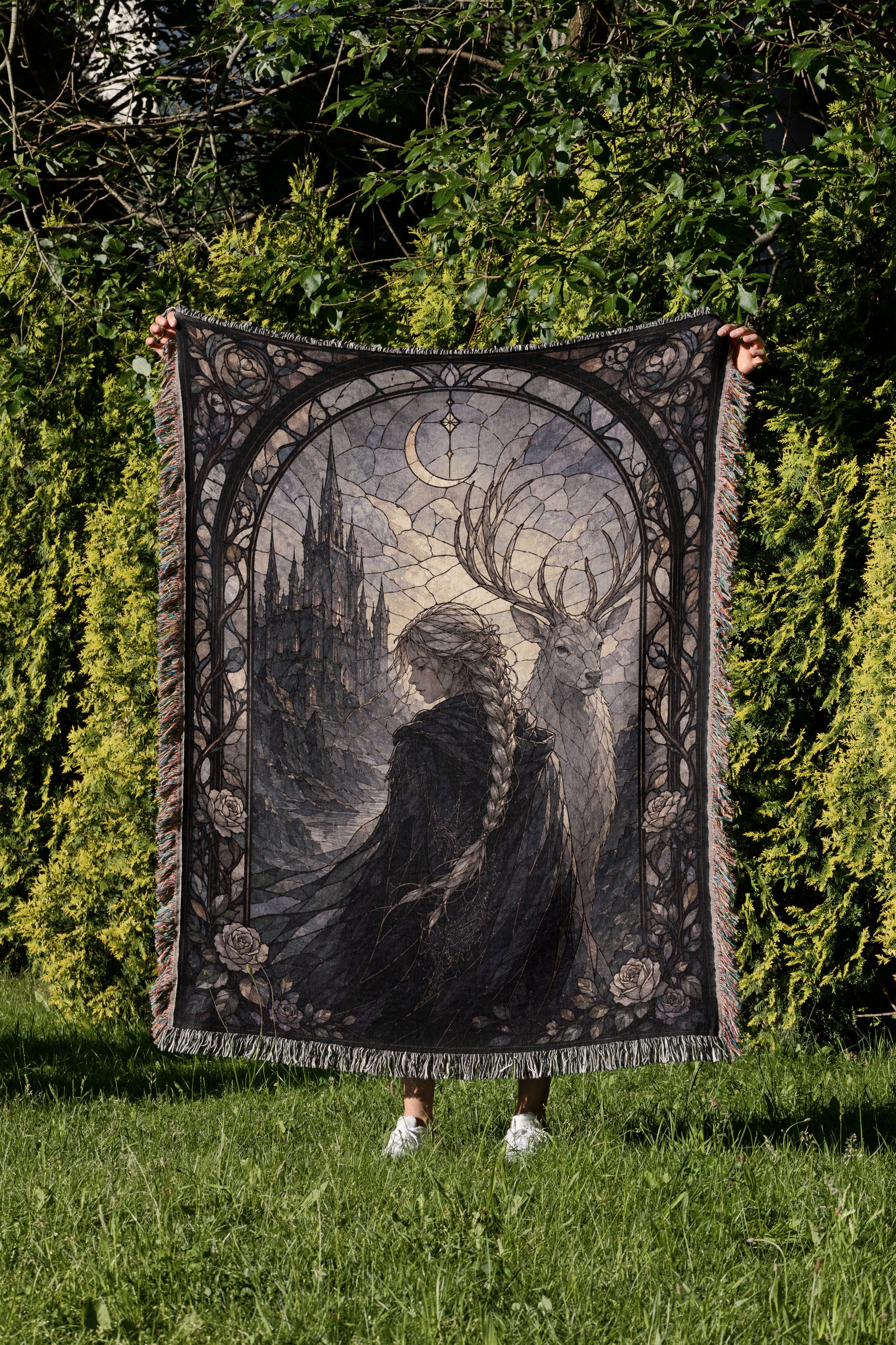 A person is holding up a large, ornate tapestry with a castle and deer design on it, set against a backdrop of trees and greenery.