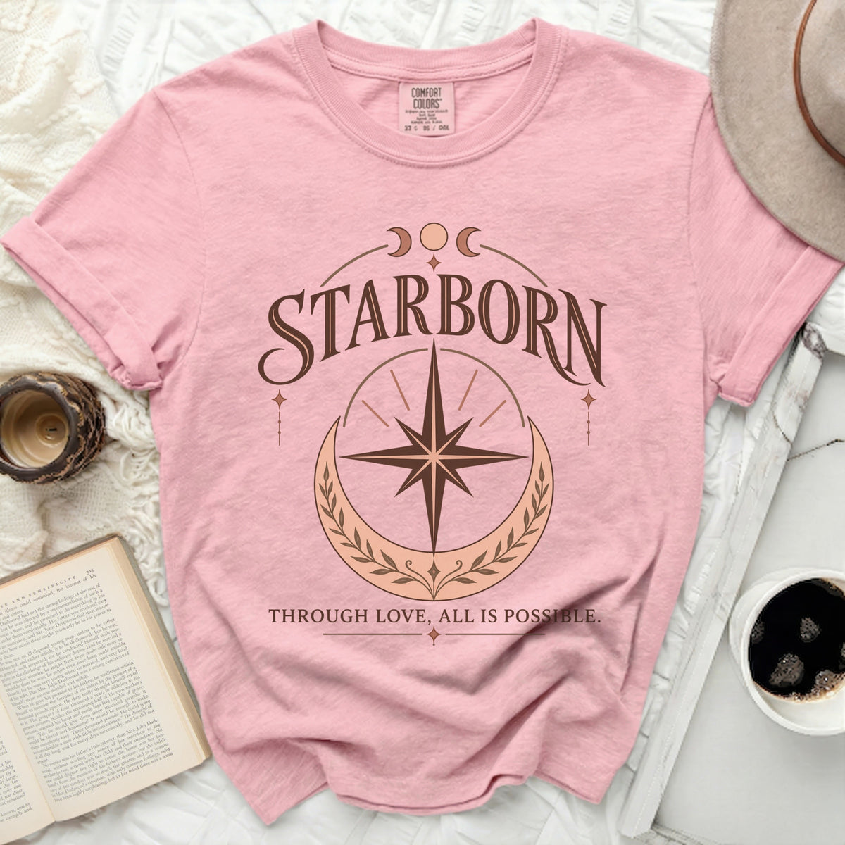 Pink t-shirt with "STARBORN THROUGH LOVE, ALL IS POSSIBLE" text and celestial graphics.