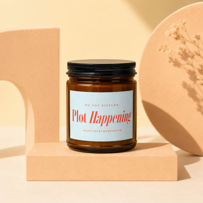 Amber glass candle with black lid, "Plot Happening" label in red text.